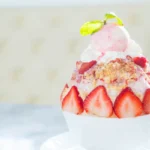 A bowl of homemade strawberry shortcake ice cream, with visible chunks of fresh strawberries and sponge cake pieces.